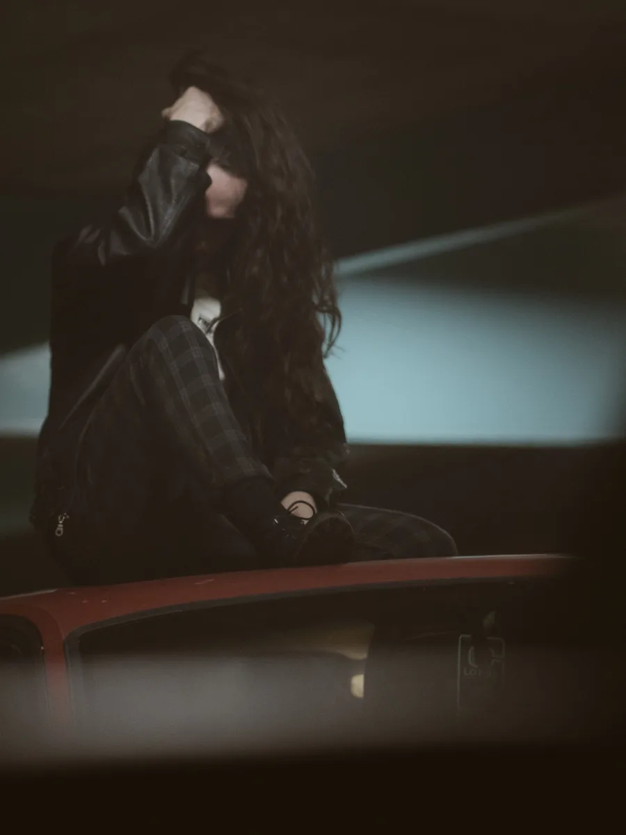 Moody portrait of a woman sitting on a car roof in a parking garage