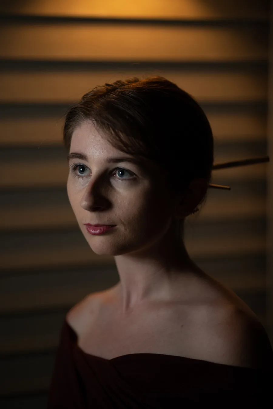 Studio portrait of a woman with a hairpin, lit warmly against window blinds